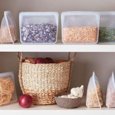 Kitchen storage bags with food inside on kitchen shelf and grass baskets with onions and garlic