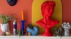 A mantel display of houseplants, candles and a colorful bust