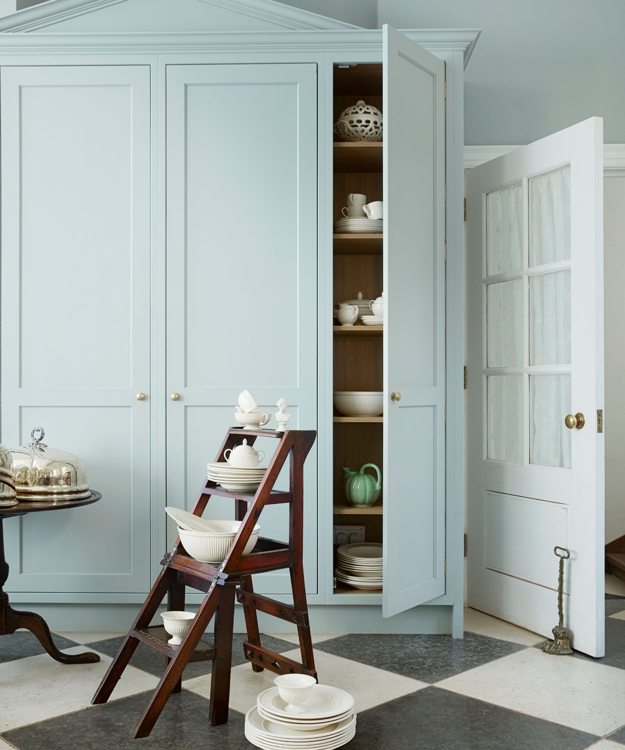 Pale blue pantry with checkerboard tile floor and a wooden ladder shelf with white crockery