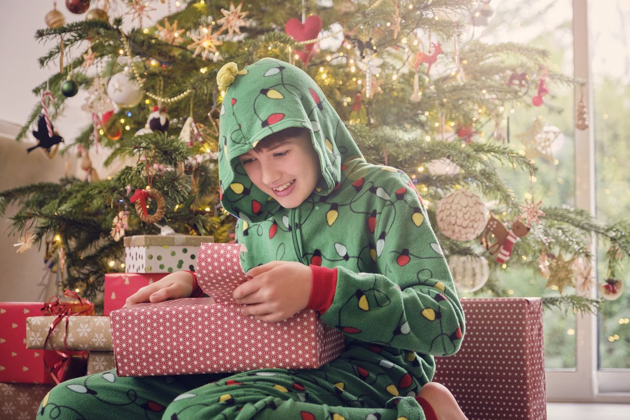 Excited boy in hooded romper tearing wrapper of gift at home during Christmas
