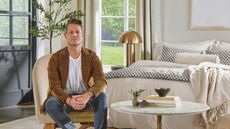 Interior designer Nate Berkus sitting in a bedroom wearing a brown jacket