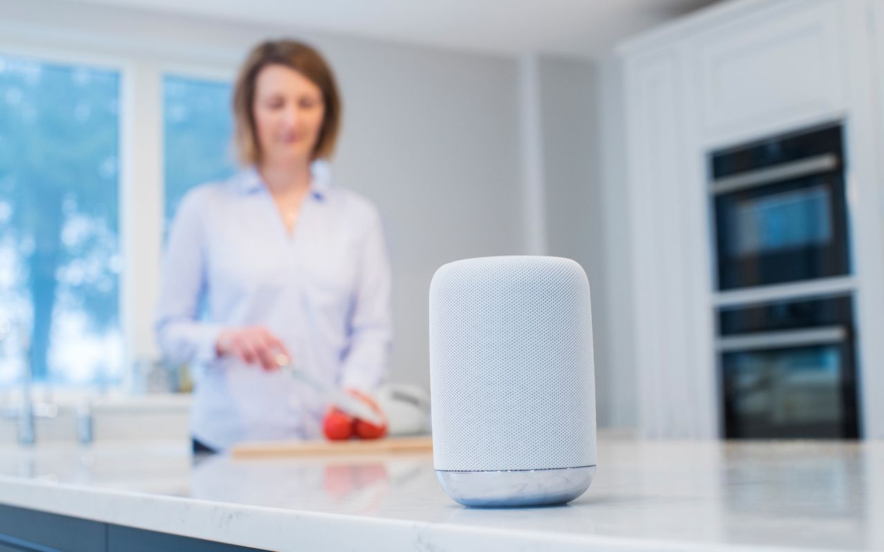 Woman Working In Kitchen With Smart Speaker In Foreground