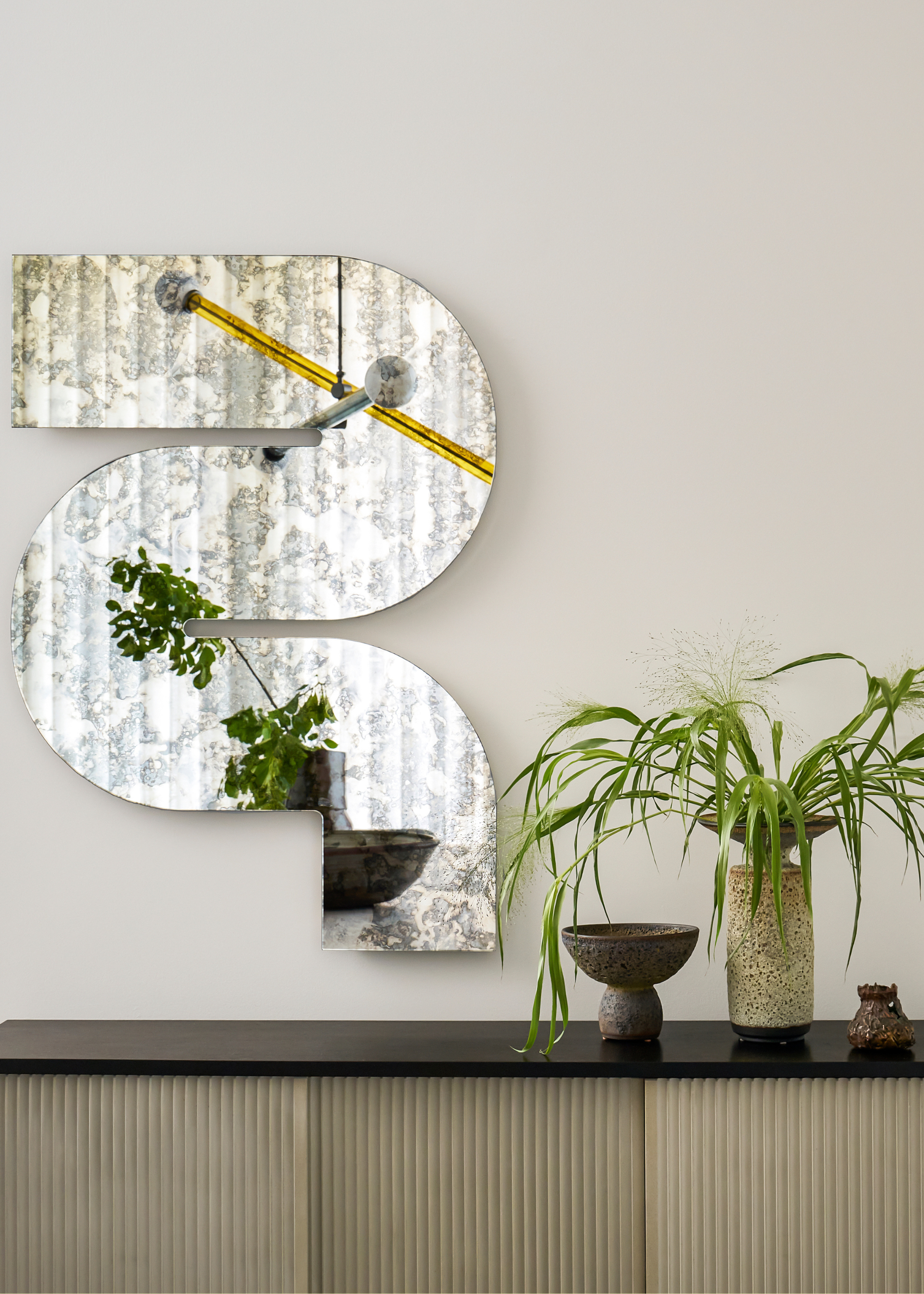 A curved wall mirror, a sideboard, a vase of stems, and a candle