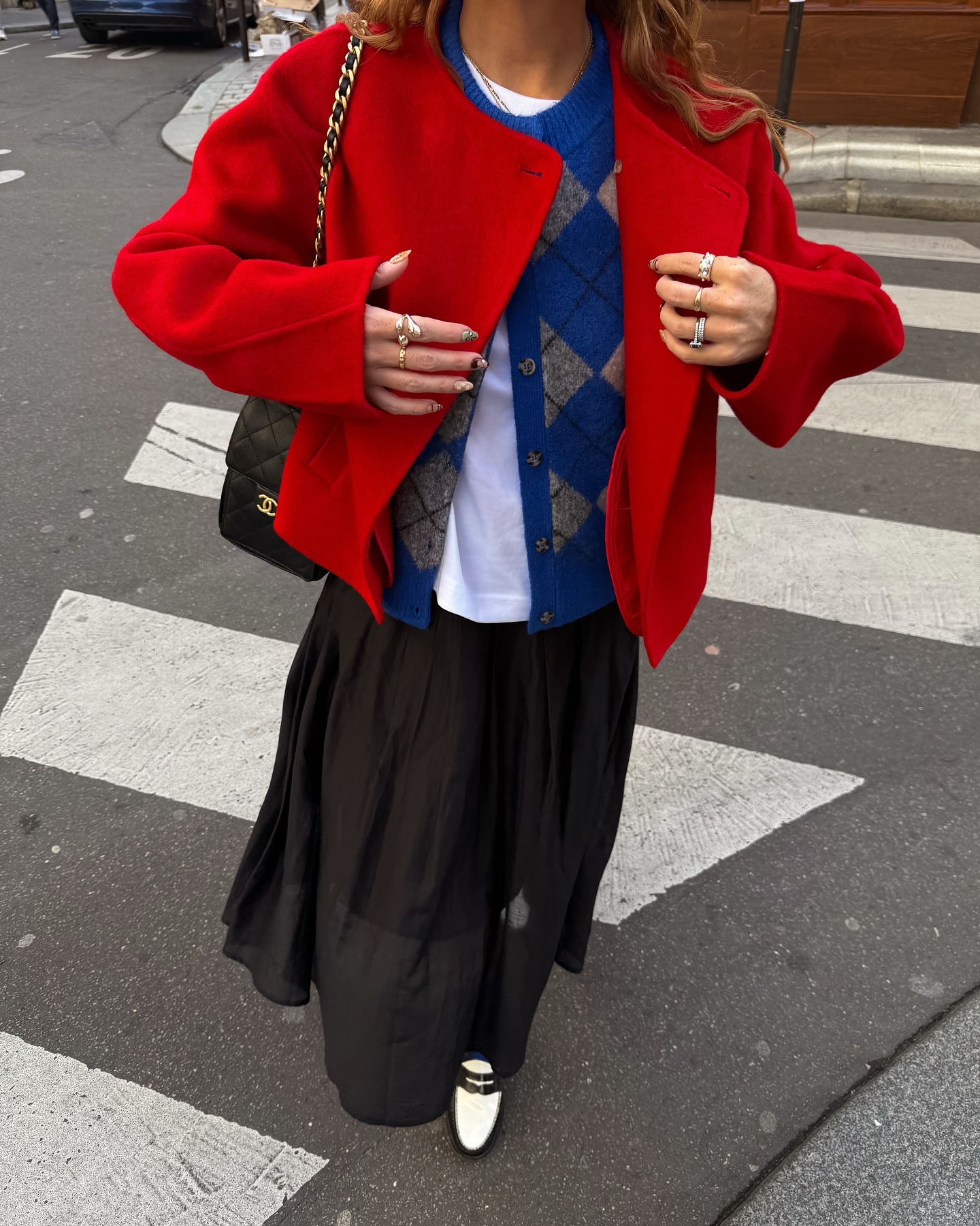 Close-up image of influencer @rebeccaferrazwyatt wearing a blue argyle cardigan over a white t-shirt with a black skirt and red jacket.