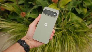 Pale green Google Pixel 11 Pro XL held in one hand against a background of green foliage.