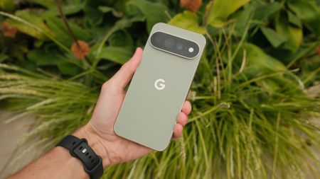 Pale green Google Pixel 11 Pro XL held in one hand against a background of green foliage.