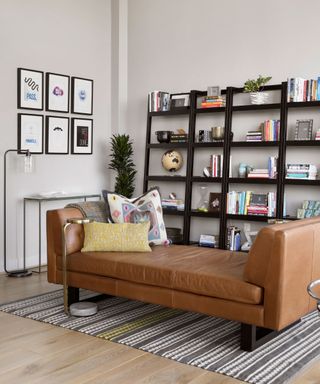 MCM lounge with tan leather chaise, striped rug, and open-shelving unit filled with colorful books.