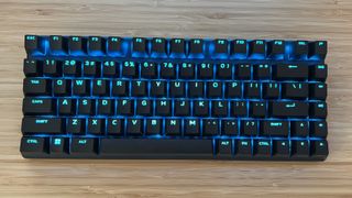 Alienware Pro Wireless gaming keyboard on a wooden desk with blue RGB