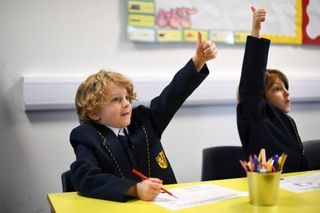 Primary school students with hands raised as schools go back in England, amid talks of a five term school year