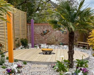 circular decked patio space surrounded by pebbles and tropical planting