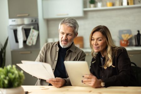 Senior couple focusing on digital tablet and physical documents while planning home budget