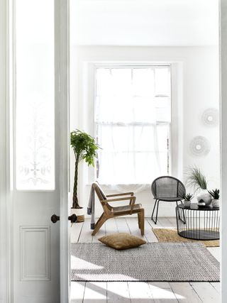 A living room with an all-white scheme by Debenhams, with black and wooden furniture and a potted plant