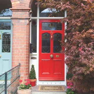 red front door in a brick porch with an acer tree wrapping around it