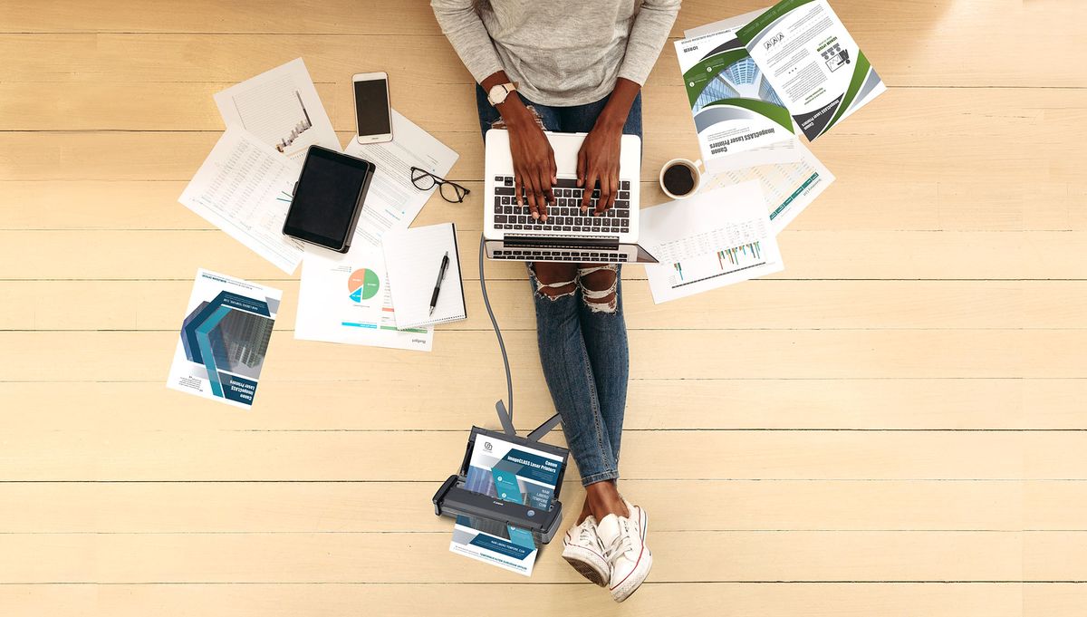 Top view of a woman entrepreneur working on laptop sitting at home. Woman sitting on floor at home working on laptop computer with coffee and business papers by her side.