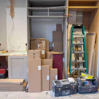 Empty cupboards, exposed wiring, stacks of cardboard boxes, ladder and toolboxes