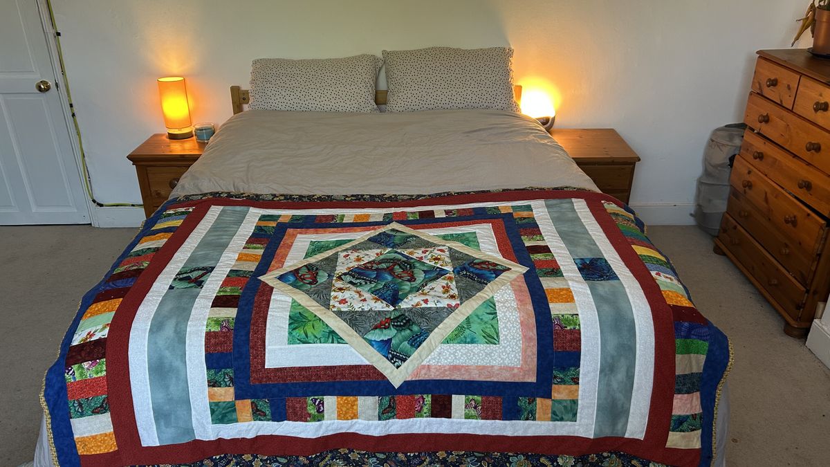 The DreamCloud Luxe Memory Foam mattress dressed in grey bedding with a colorful throw.