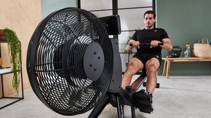 best rowing machines: pictured here, an athletic man using a rowing machine in a living room