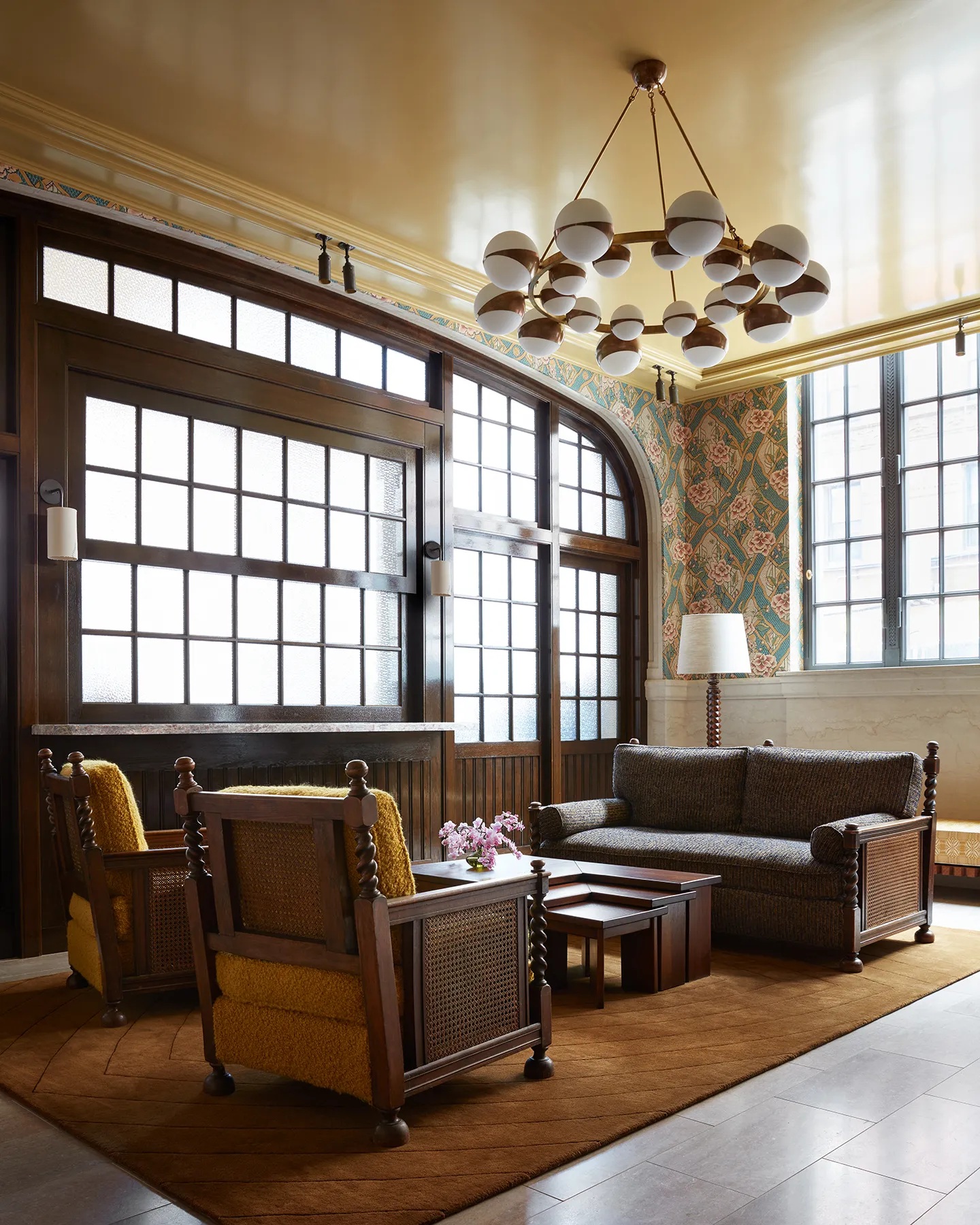 A modern glamour New York hotel boasts spherical Art Deco lighting paired with ornate walls filled with artworks and wooden cabinetry, all infused with soft pastels.