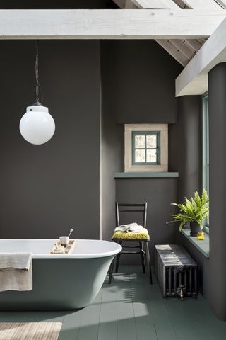 A dark gray bathroom with green woodwork and a green bath, green floor, and white pendant light