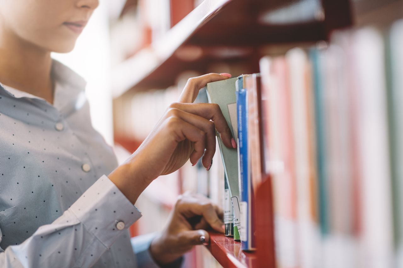 Woman at the library, she is searching books on the bookshelf and taking a textbook on the shelf, hand close up