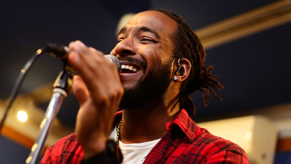 Male singer holds wearing a red shirt with in-ear monitors in his ears