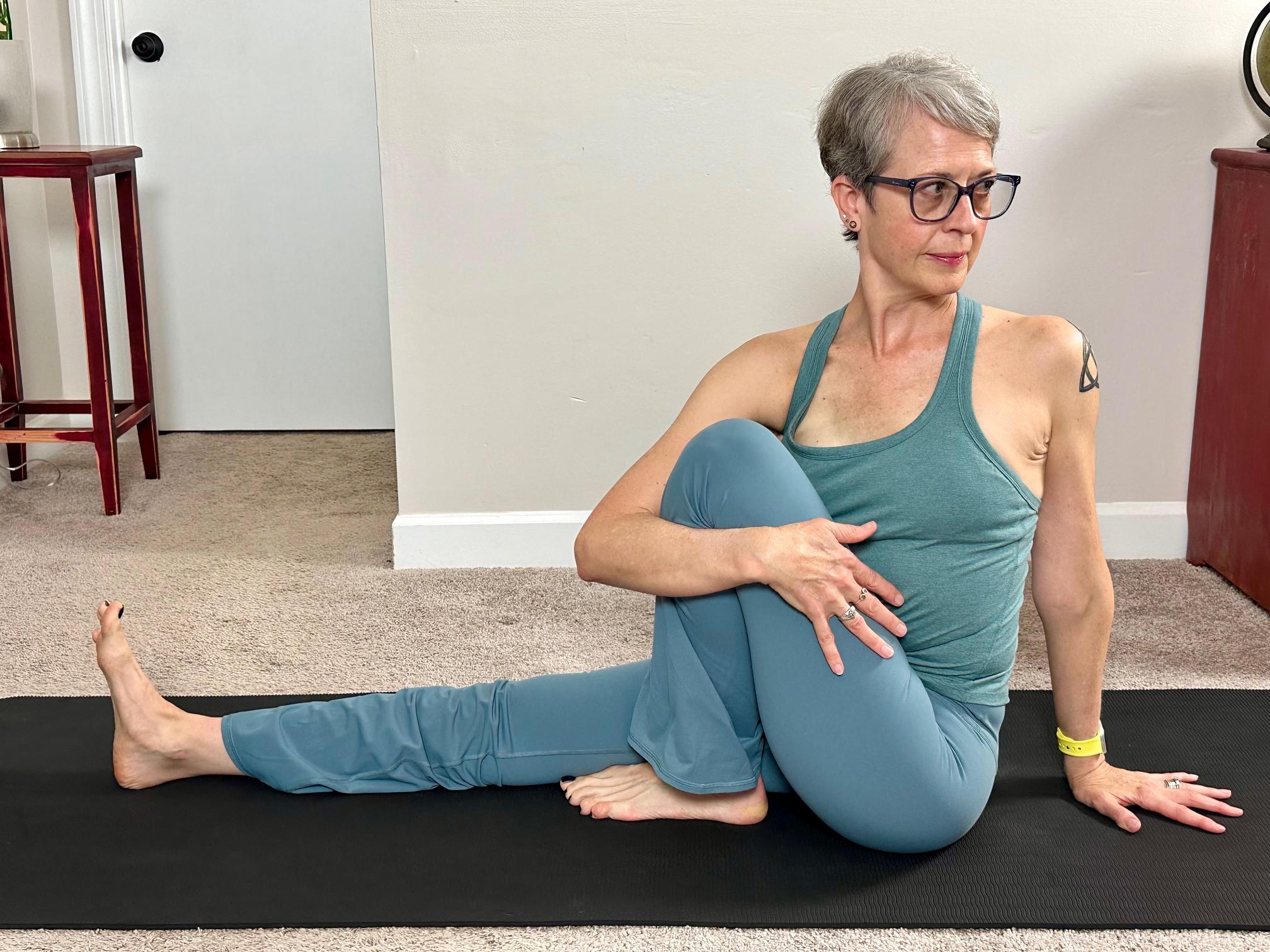 woman performing a seated yoga twist on the floor with one leg extended and the other bent