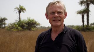 Martin Clunes in a black shirt against a backdrop of palm trees in Martin Clunes: Islands of the Atlantic