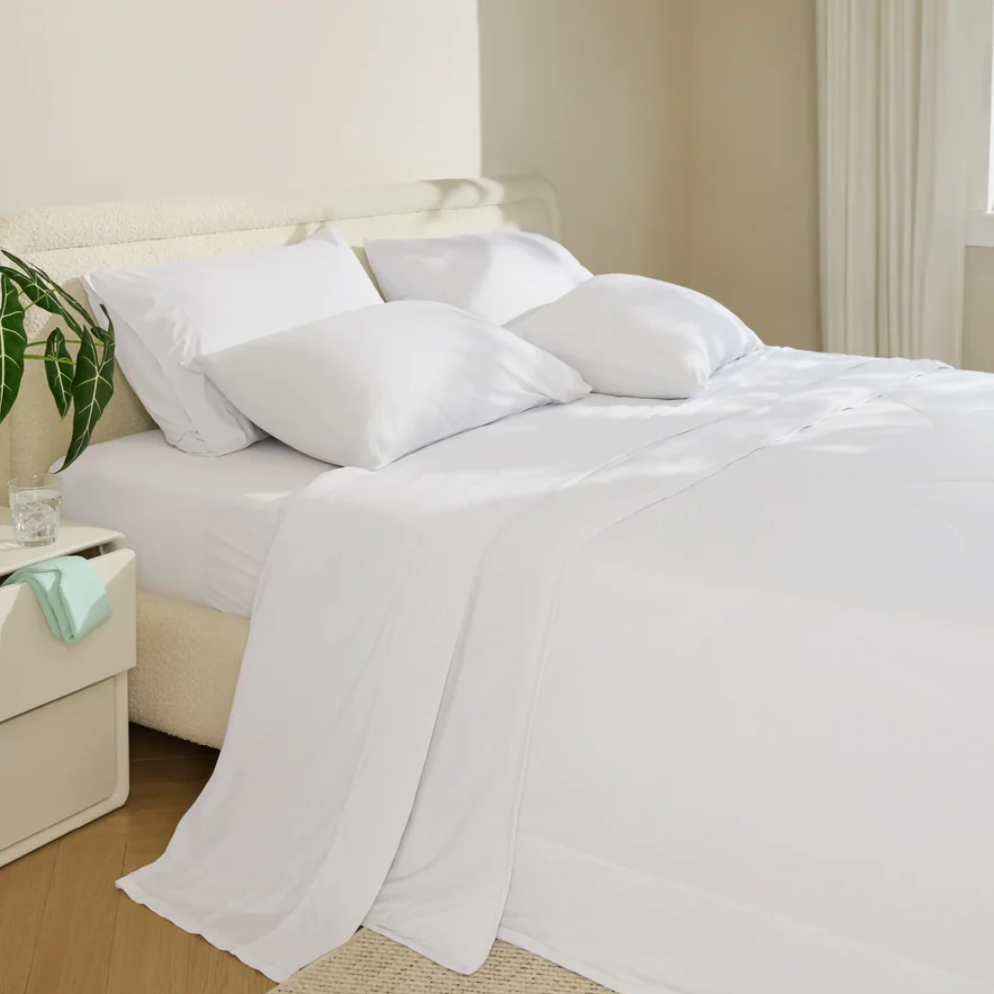 a bedroom with white sheets, four pillows, and a night stand with an open drawer on the left side of the bed