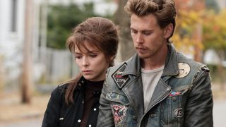 Jodie Comer and Austin Butler stand together looking somber in The Bikeriders.