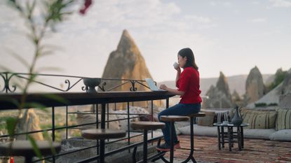 A young female freelancer tourist is using her laptop at the rooftop patio of the hotel where she is staying during her travel.