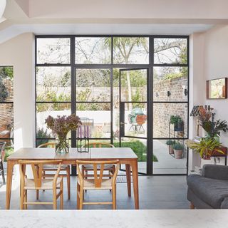 A contemporary kitchen-diner-living space with wooden dining table and Crittal-style black-framed doors looking out onto back garden