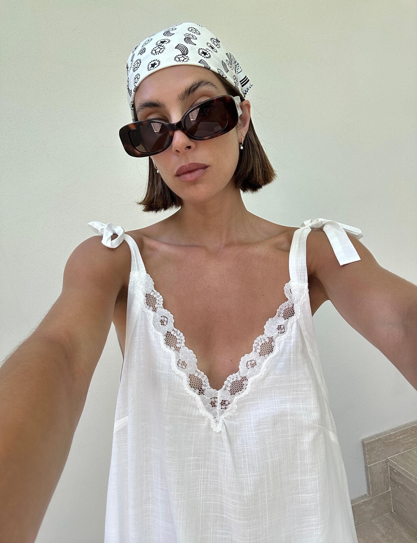 Fashion person Jamie Ridge wears a silk scarf on a recent trip abroad. She pairs it with a white linen dress and rectangle sunnies in a image taken from her Instagram.