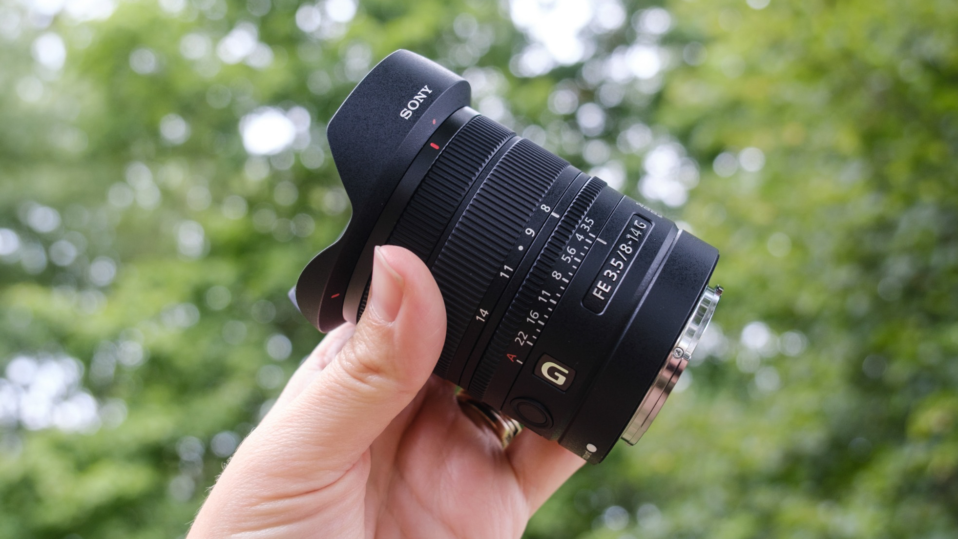 Sony FE 8-14mm f/3.5 Fisheye lens being held in a woman's hand outdoors