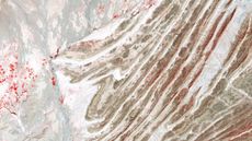 A false-color satellite photo of a series of alternating rocky folds across the landscape