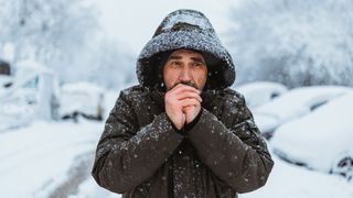 Portrait shot of the caucasian good looking mature man in casual style is freezing on the cold winter day while standing in the center city.