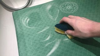 A yoga mat being cleaned in a bath tub with soapy water