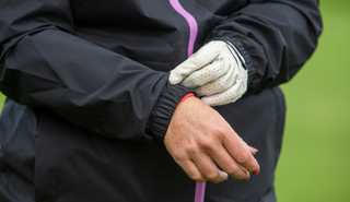 A golfer adjusts the sleeves of the adidas Women's Rain.RDY Golf Jacket