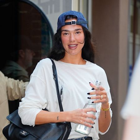 Dua Lipa wearing a white tee, jean shorts, ballet flats, and a baseball cap 