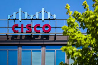 A building with a red Cisco sign displayed on its roof is visible through the green leaves of a tree