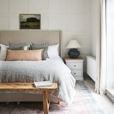 A cream bedroom with a taupe headboard and bed dressed in neutral bed linen