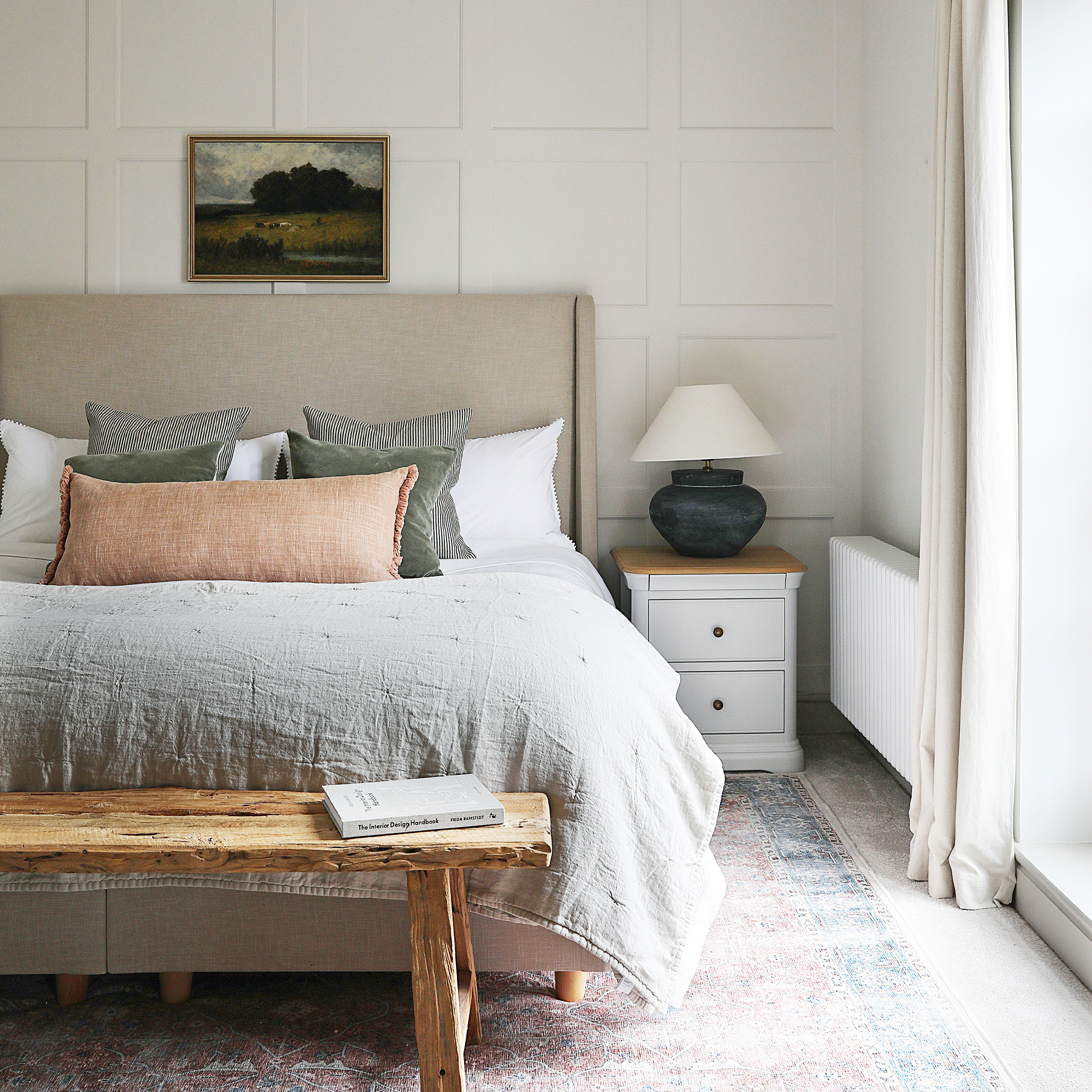 A cream bedroom with a taupe headboard and bed dressed in neutral bed linen