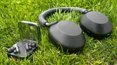 The Sony WH-1000XM5 laying on the ground next the Nothing Ear wireless earbuds.