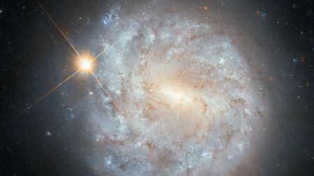 a spiral galaxy and a bright star appear to overlap in a hubble space telescope image