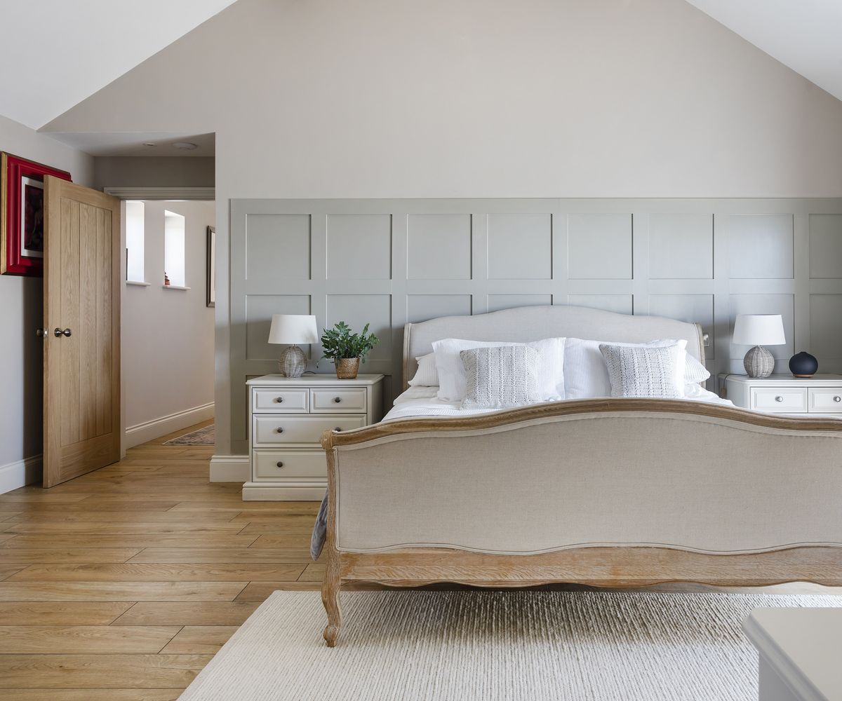 A modern but traditional bedroom with pale green panelling and a wooden floor with cream large double bed