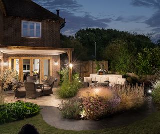 A garden in the darkness illuminated with multiple levels of outdoor lighting on an arbour and in flower beds