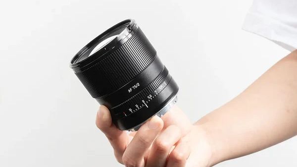 The TTArtisan 75mm f/2 lens held in a hand on a white background