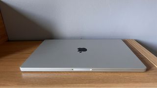 Image shows a closed MacBook Pro M1 Pro 2021 on a wooden table.