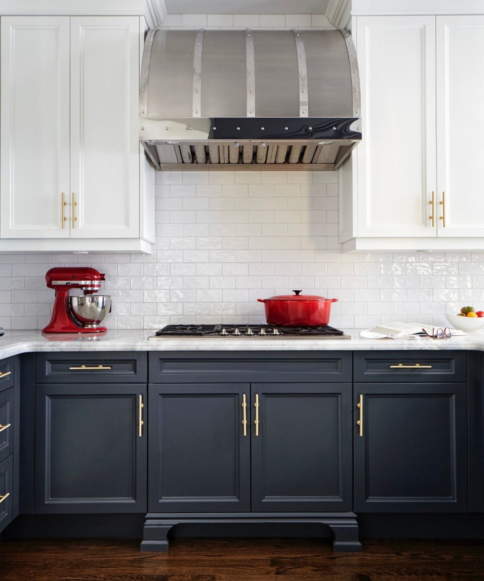 kitchen with dark navy lower cabinets, white tiles and upper cabinets, red cookware