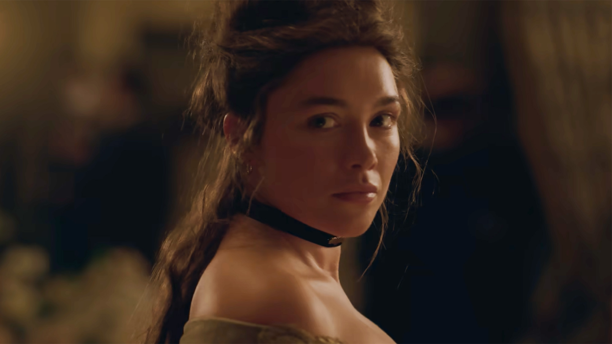 Florence Pugh looks back behind her with a black ribbon choker around her neck. Her hair is in an updo.