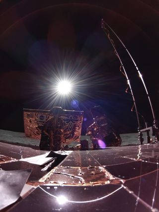 a bright sun can be seen in a totally black sky above solar panels and antennae. the grey, dusty surface of the moon can be seen extending into the background